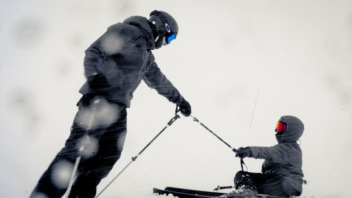 Un esquiador ayuda a otro a levantarse tras una caída en la nieve, sujetando los bastones entre ambos
