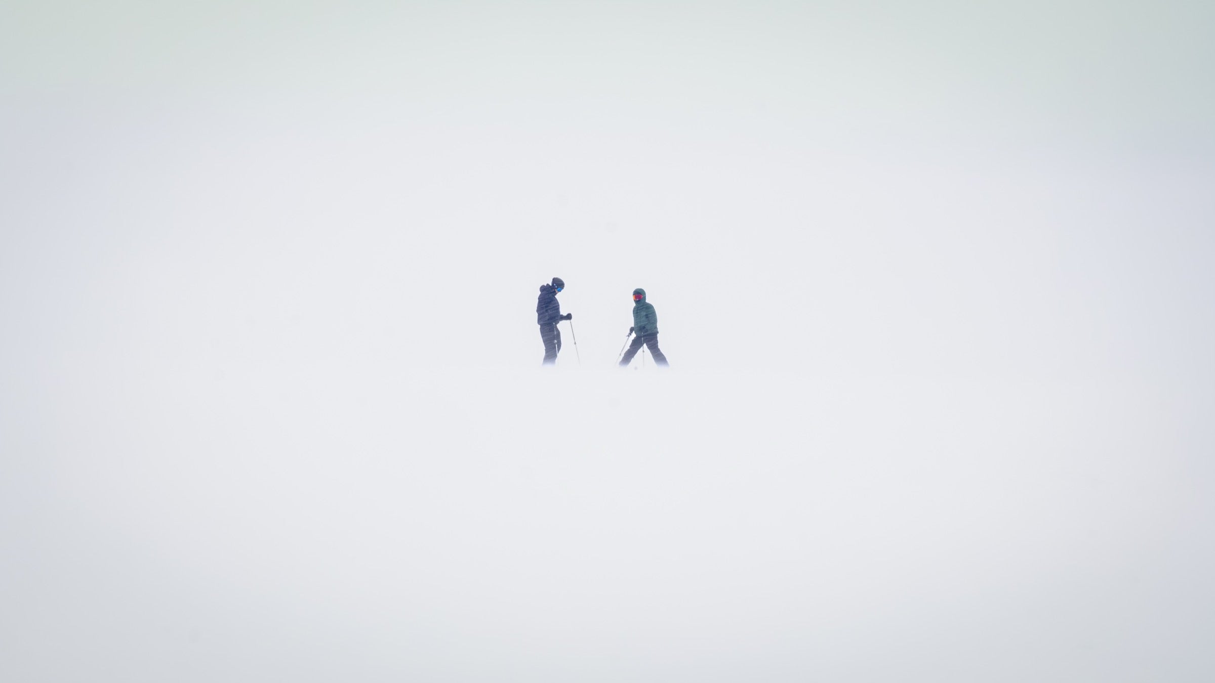Dos esquiadores de pie conversando, como siluetas pequeñas en medio de la niebla blanca de Corralco